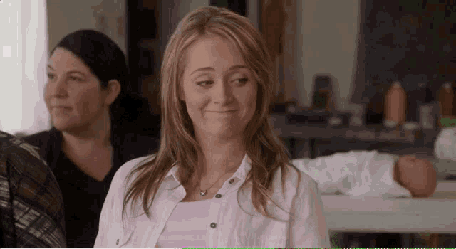 a woman in a white shirt is smiling in front of another woman