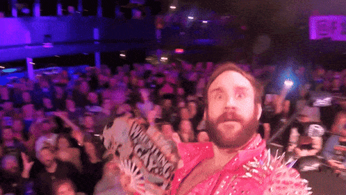 a bearded man in a pink jacket holds a sign that says " when i win "