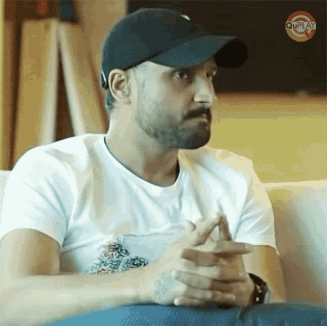 a man wearing a black hat and a white t-shirt is sitting on a couch