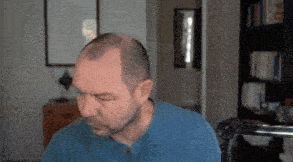 a man with a bald head is sitting in front of a microphone in a living room .