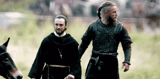 two men are walking in a field with a horse .
