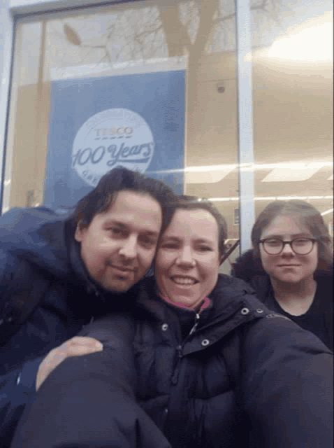 a man and two women pose for a picture in front of a sign that says tesco 100 years
