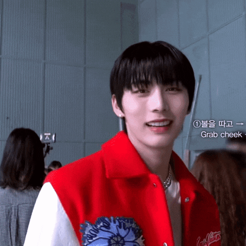 a young man wearing a red jacket says grab cheek in a foreign language
