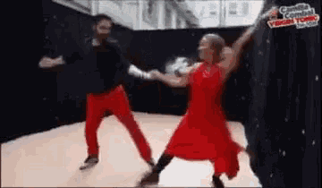 a man and a woman are dancing together on a dance floor . the woman is wearing a red dress .