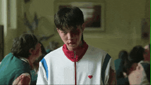 a young man with blood on his face is wearing a white jacket with a heart on the front .