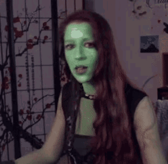 a woman with a green mask on her face is wearing black gloves and making a funny face .