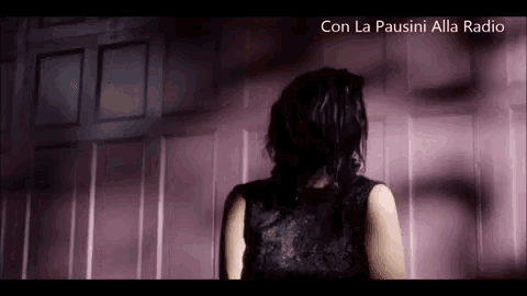 a woman in a black lace dress is standing in front of a pink wall .