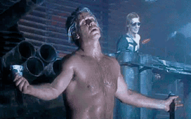 a man without a shirt is standing in a dark room with his arms outstretched and a cup in his hand .