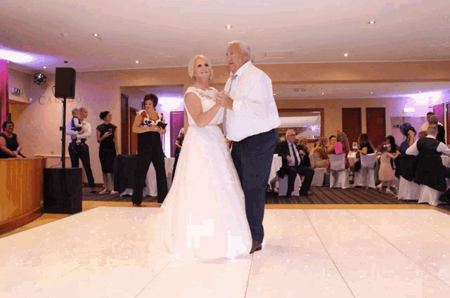 a bride and groom are dancing on a white floor