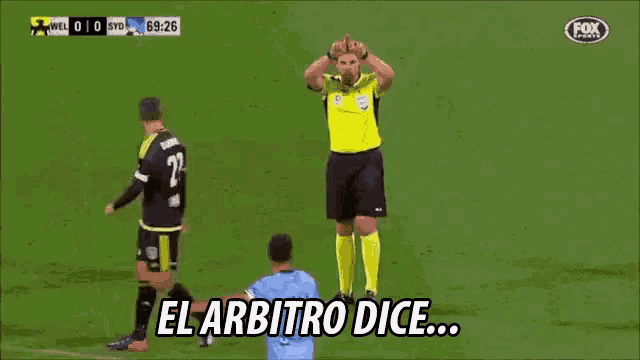 a soccer referee stands on the field with his arms up and says el arbitro dice