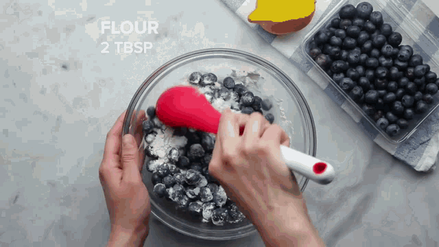 a person is mixing blueberries with flour in a glass bowl
