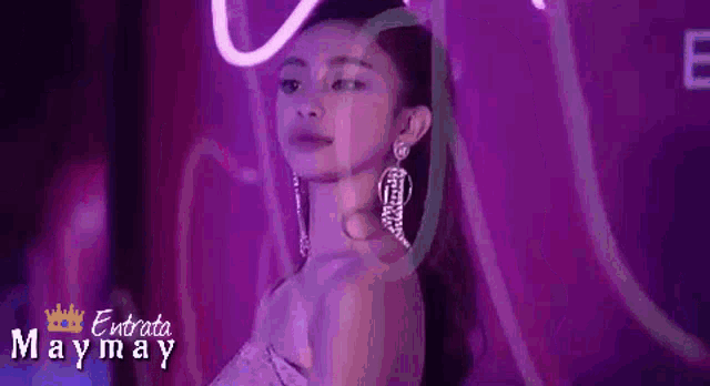 a woman in a purple dress and earrings is standing in front of a purple light .