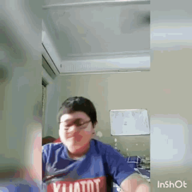 a young boy wearing glasses and a blue shirt is making a funny face in a bedroom .