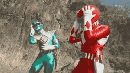 a red power ranger is standing next to a green power ranger in a field .