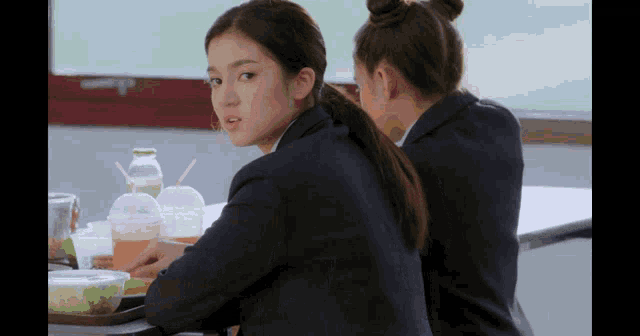 two girls sit at a table with plastic cups of drinks