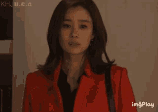 a woman in a red coat is standing in front of a bookshelf and a speaker with imgplay written below her