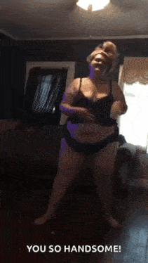a woman in lingerie is dancing in a living room and says you so handsome .