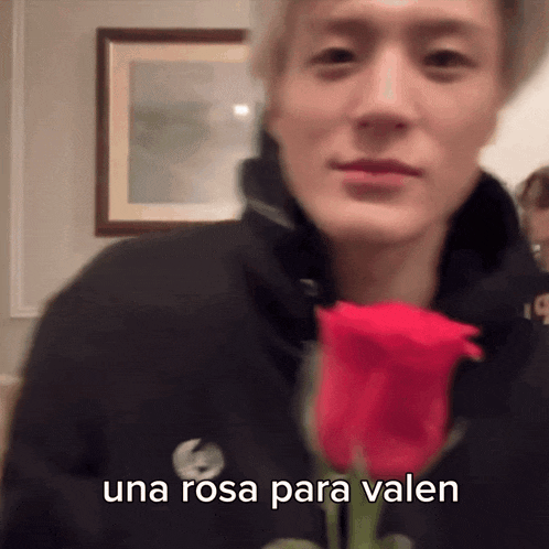 a man in a black hoodie is holding a red rose with the words una rosa para velen below him