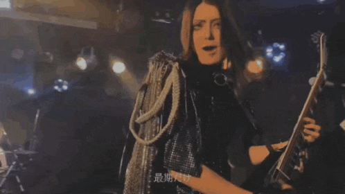a woman in a black jacket is holding a guitar and giving the middle finger