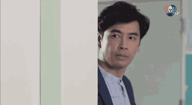 a man in a suit and tie is peeking out of a doorway .