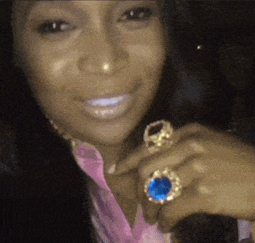a woman wearing a pink shirt and gold rings on her fingers