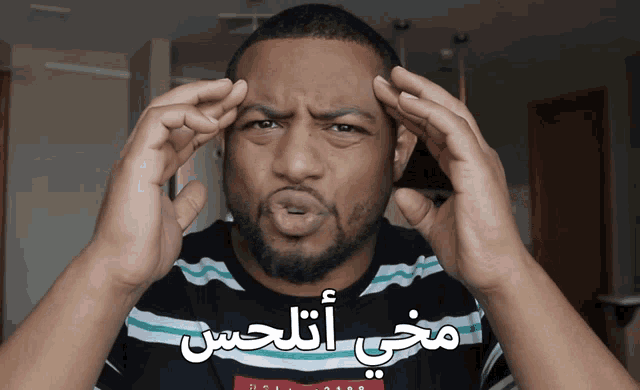 a man with arabic writing on his shirt holds his hands to his head