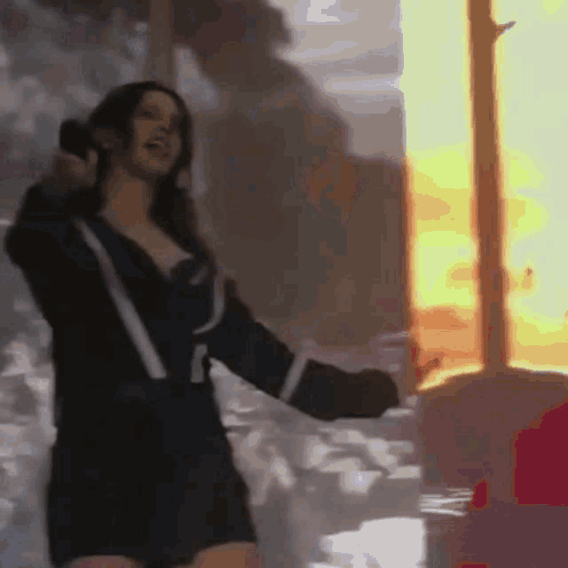 a woman in a black dress is standing in front of a fire