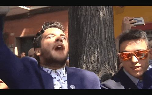 a man wearing sunglasses is taking a picture of another man in a suit