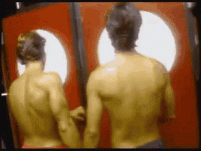 two shirtless men standing next to each other in front of a red door