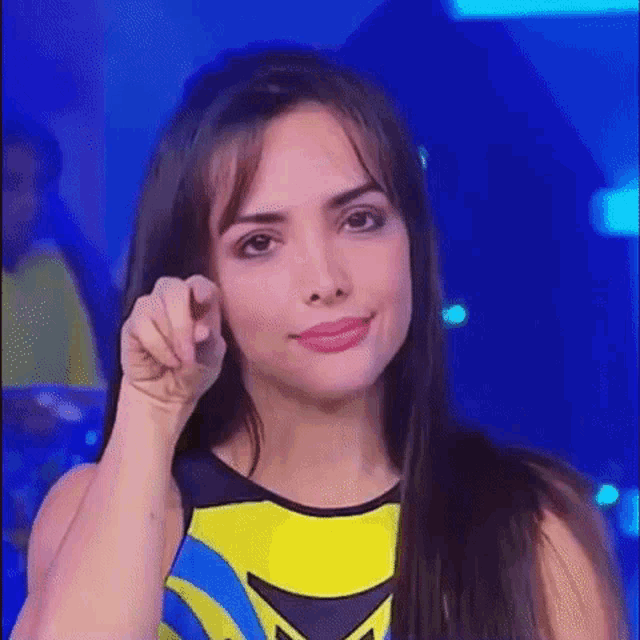 a woman is pointing at the camera while wearing a yellow and blue outfit .