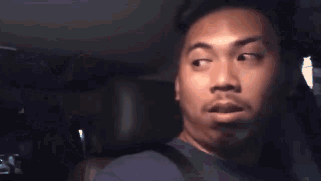 a man is making a funny face while sitting in the back seat of a car at night .