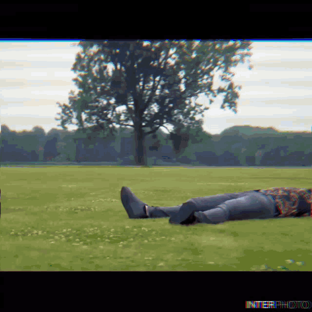 a person is laying in the grass with a tree in the background and the words interphoto below them