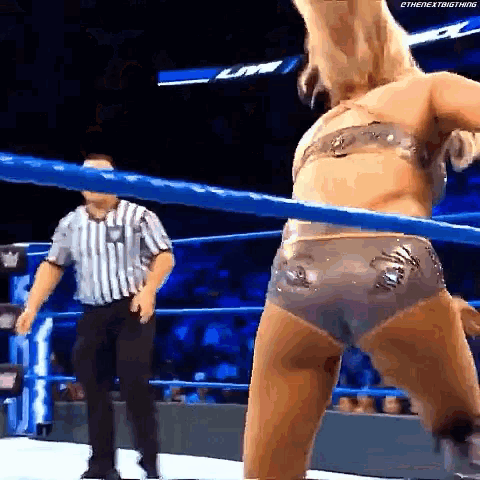 a woman in a bikini is standing in a wrestling ring with a referee standing behind her .