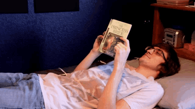 a man laying on a bed reading a book called the princess bride