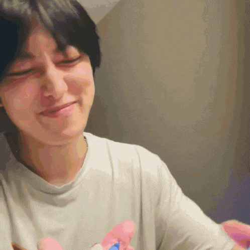 a man in a white shirt is smiling and holding a pink and blue toy .