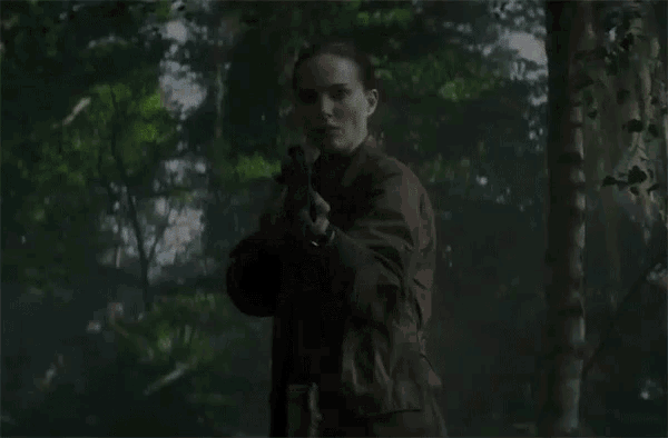 a woman is holding a gun in the woods and looking at the camera .