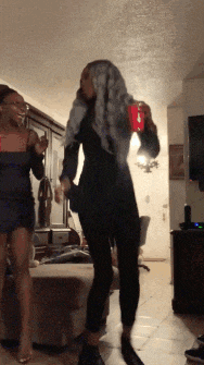 two women are dancing in a living room while one holds a red cup