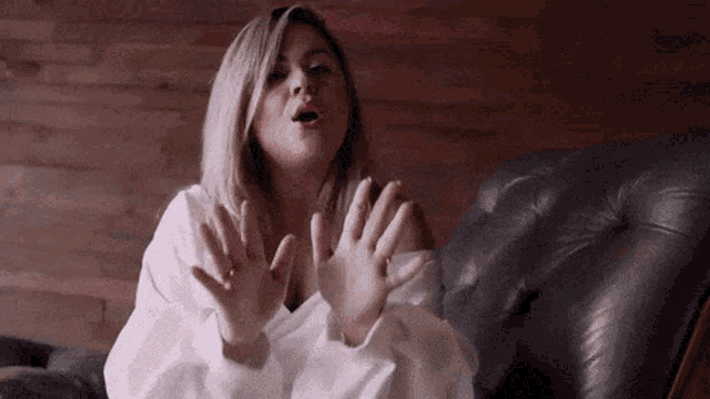 a woman in a white shirt is sitting in a chair with her hands outstretched .