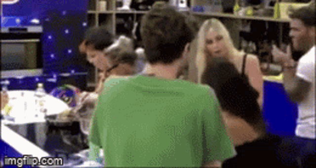 a man in a green shirt is standing in front of a group of people in a room .