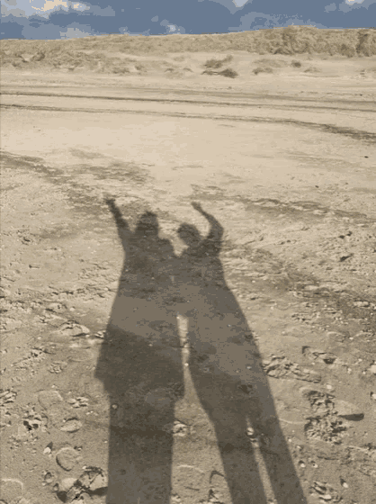 a couple 's shadows are cast on the sand on a beach