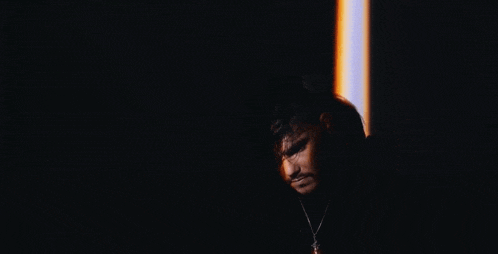 a man with a beard is standing in the dark with a light shining on his face .