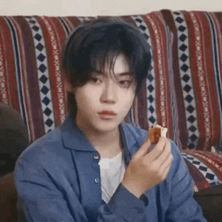 a young man is sitting on a couch eating a sandwich .