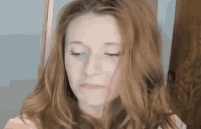 a woman with long red hair is making a sad face with her eyes closed .