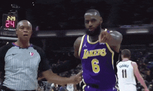 a basketball player wearing a lakers jersey is pointing at a referee
