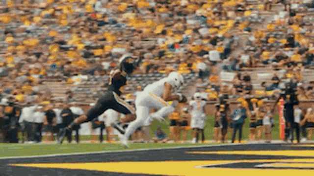 a football player is jumping in the air to catch a ball while another player runs after him .