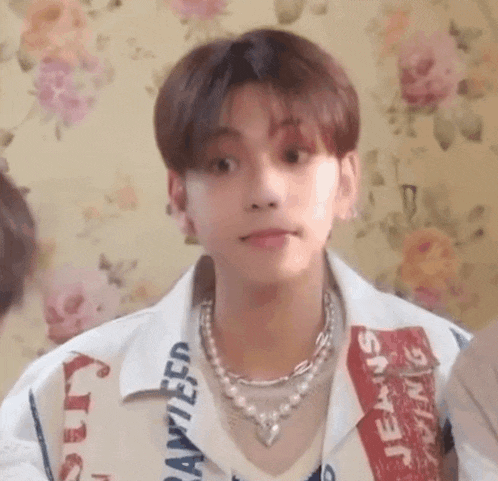 a young man wearing a pearl necklace and a white shirt is making a face .