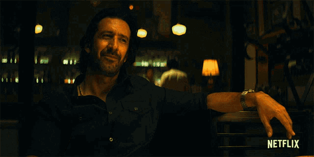 a man sits at a table with a glass of whiskey in front of a netflix sign