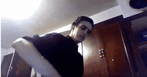 a man in a black shirt is standing in a kitchen with wooden cabinets