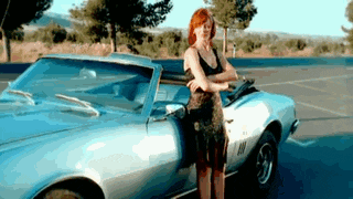 a woman in a black dress is standing next to a silver car in a parking lot