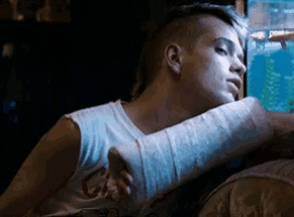a young man with a cast on his arm is laying on a couch in front of an aquarium